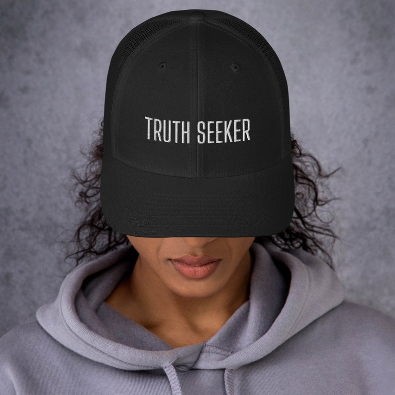May include: A black mesh trucker hat with a white embroidered inscription that reads "TRUTH SEEKER".