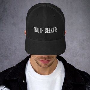 May include: A black mesh trucker hat with a white embroidered design that says "TRUTH SEEKER".