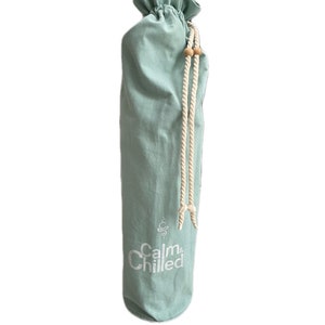 May include: A light blue canvas yoga mat bag with a drawstring closure and white rope handles. The bag has the text "Calm & Chilled" printed on the front in white.