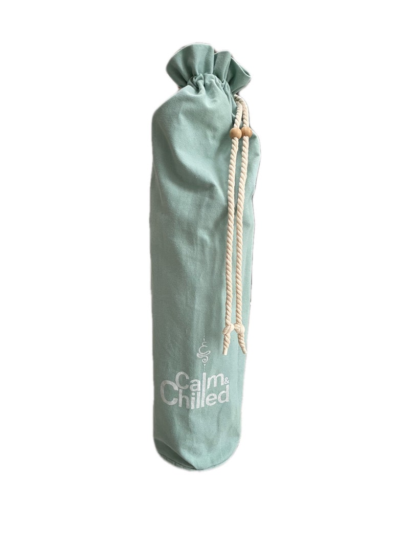 May include: A light blue canvas yoga mat bag with a drawstring closure and white rope handles. The bag has the text "Calm & Chilled" printed on the front in white.
