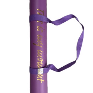 May include: Purple yoga mat with a gold inscription that reads "This is my workout". The mat has a purple carrying strap.