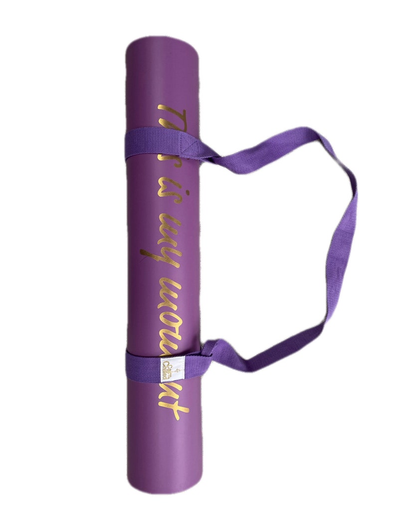 May include: Purple yoga mat with a gold inscription that reads "This is my workout". The mat has a purple carrying strap.