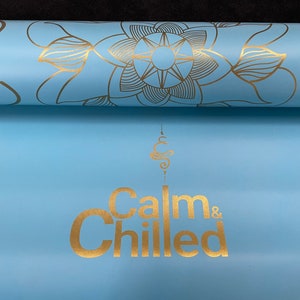 May include: A light blue yoga mat with a gold mandala design and the text "Calm & Chilled" in gold lettering.