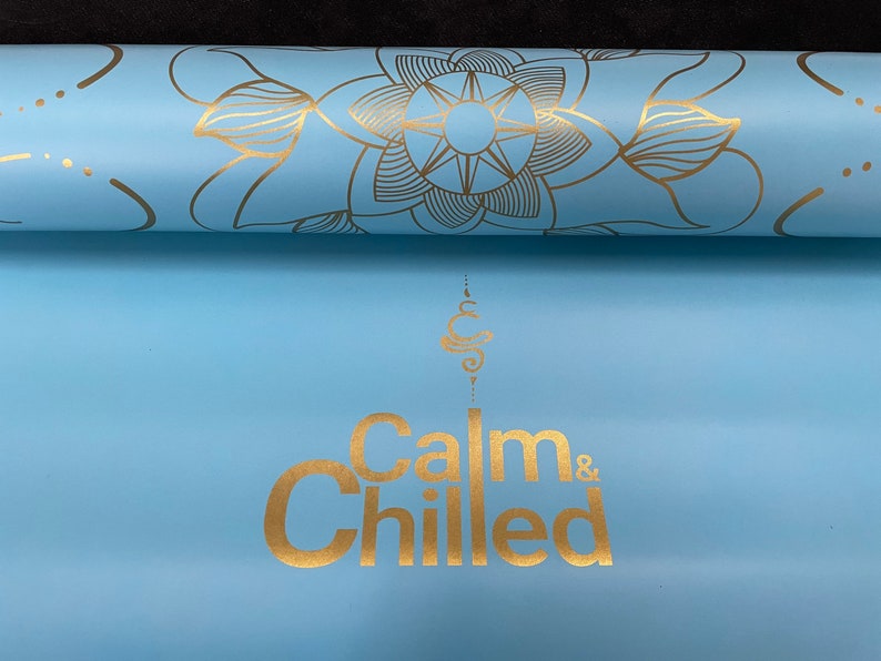 May include: A light blue yoga mat with a gold mandala design and the text "Calm & Chilled" in gold lettering.