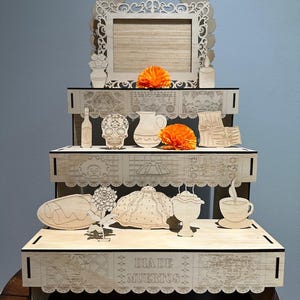 May include: A wooden Day of the Dead altar with multiple shelves, adorned with laser-cut decorative elements. The altar features a central frame, various cut-out objects, and vibrant orange flowers. The phrase "DIA DE MUERTOS" is visible on the front.