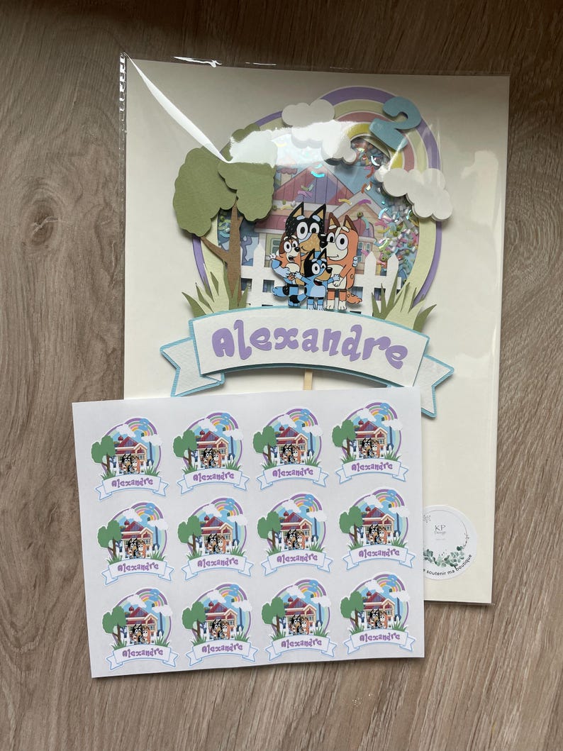 K&ouml;nnte beinhalten: Ein Satz mit 12 runden Aufklebern mit einem Cartoon-Bild eines Hauses mit einem Regenbogen und dem Namen "Alexandre" auf einem Banner. Die Aufkleber sind auf wei&szlig;em Papier mit gl&auml;nzender Oberfl&auml;che gedruckt.