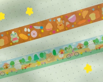 May include: An open notebook with three decorative washi tape rolls featuring food and nature-themed designs. A clear acrylic keychain with a cartoon character is in the lower left corner. Yellow star stickers are scattered across the notebook pages.