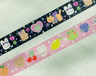 May include: Three decorative washi tapes with repeating patterns of cute cartoon characters and objects. One tape is black with white, purple, and green designs. Another is pink with fruit and animal designs. The third tape is black with a repeating pattern.