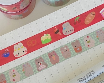 May include: An assortment of decorative washi tape rolls and strips featuring cute bear and bunny illustrations with food and floral designs. Two white double-ended Mildliner pens are also visible on a spiral notebook.