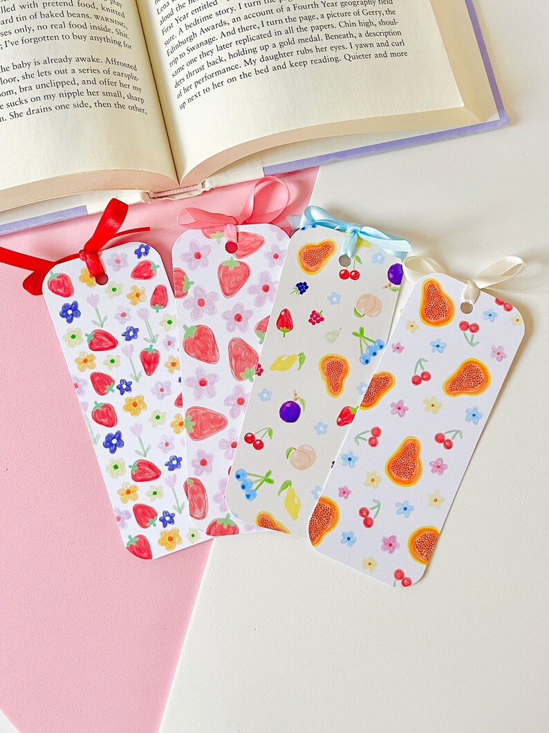 Puede incluir: Cuatro marcap&aacute;ginas coloridos con dise&ntilde;os de frutas y flores. Cada marcap&aacute;ginas presenta un patr&oacute;n diferente de fresas, cerezas, ar&aacute;ndanos y papaya. Est&aacute;n atados con cintas rojas y azules, y est&aacute;n junto a un libro abierto.