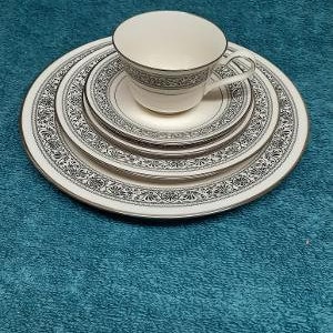 May include: A set of four white ceramic plates with black floral designs and a white ceramic teacup with a black band around the top.