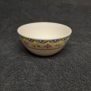 May include: A white ceramic bowl with a floral design in shades of blue, green, and pink. The bowl has a rounded shape and a wide rim.