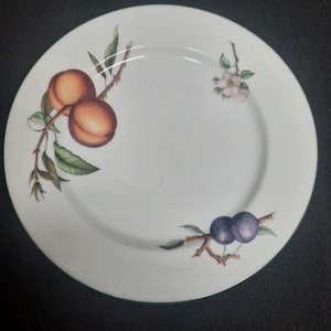 May include: A white ceramic dinner plate with a green rim features a painted design of peaches, plums, and a flower. The peaches are orange and red, the plums are purple, and the flower is pink with green leaves.