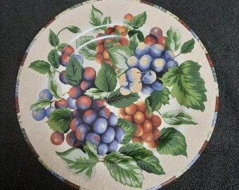 May include: A white ceramic dinner plate with a colorful grapevine design. The plate features green leaves, purple grapes, and red berries.