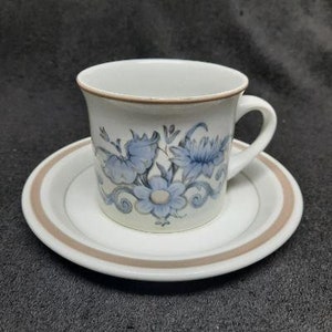 May include: A white teacup and saucer set with a floral design. The cup has a brown rim and a blue and white floral pattern. The saucer has a brown rim and a white center.