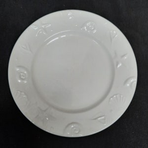 May include: White ceramic plate with a raised design of seashells and starfish around the edge.