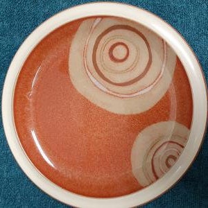 May include: A ceramic bowl with a white rim and a red interior. The bowl has a white and brown swirl design.