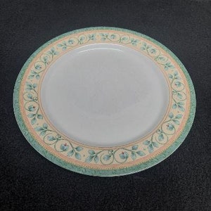 May include: A white ceramic dinner plate with a green and yellow floral design around the rim.