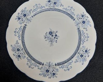 May include: A white ceramic dinner plate with a blue and white floral pattern. The plate has a scalloped edge and a raised rim.