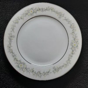May include: A white ceramic plate with a delicate floral design featuring white flowers and green leaves around the rim.