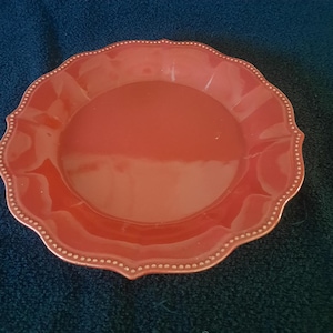 May include: A red ceramic dinner plate with a scalloped edge and a dotted design.