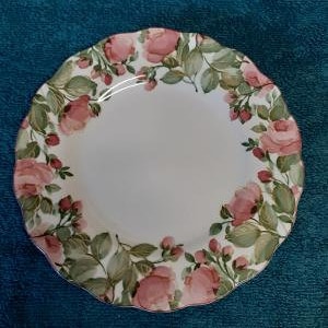 May include: A white ceramic dinner plate with a scalloped edge and a floral design featuring pink roses and green leaves.