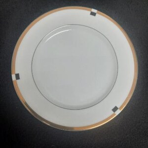 May include: A white ceramic plate with a gold rim and black squares. The plate is a simple design with a clean, modern look.