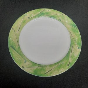 May include: A white ceramic plate with a green and yellow rim featuring a golf club design.