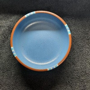 May include: A blue ceramic bowl with a brown rim and blue and white stripes around the edge.