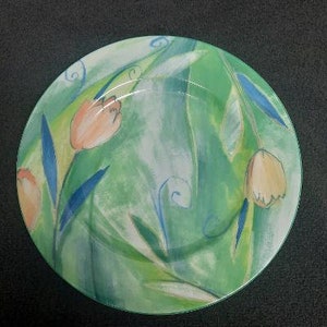 May include: A green and white ceramic plate with a floral design featuring tulips. The tulips are painted in shades of pink, orange, and yellow.
