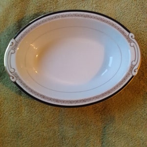 May include: White oval serving bowl with a black and gold rim and a decorative pattern.