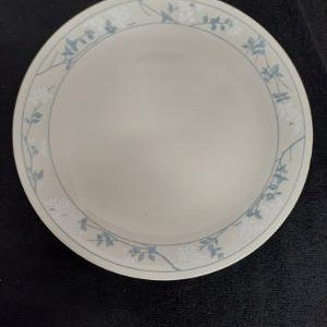 May include: A white ceramic dinner plate with a blue floral design around the rim. The flowers are stylized and have a delicate, almost watercolor-like appearance.