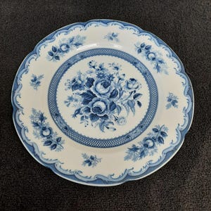 May include: A white ceramic dinner plate with a blue and white floral design. The plate has a scalloped edge and a raised rim.