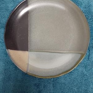 May include: A round ceramic plate with a geometric design. The plate is divided into four sections, each with a different color: black, beige, light gray, and a darker gray.
