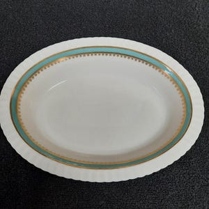 May include: White oval serving bowl with a scalloped edge. The bowl has a teal blue band with a gold trim and a gold pattern of small stars.