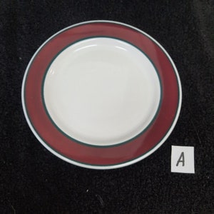 May include: A small, white ceramic plate with a red and green rim. The plate has a simple design and is perfect for serving snacks or desserts.
