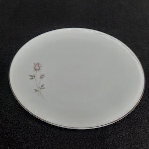 May include: A white ceramic plate with a silver rim and a delicate floral design featuring pink roses.