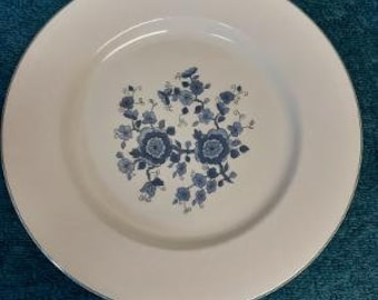 May include: A white ceramic dinner plate with a green rim and a blue floral design.