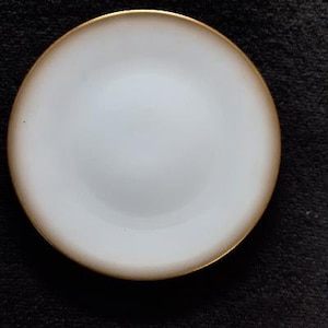 May include: A white ceramic plate with a gold rim. The plate is round and has a smooth surface.