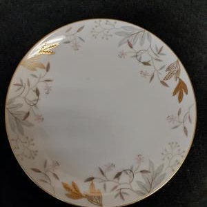 May include: A white ceramic plate with a gold rim and a delicate floral design in shades of brown and gold.