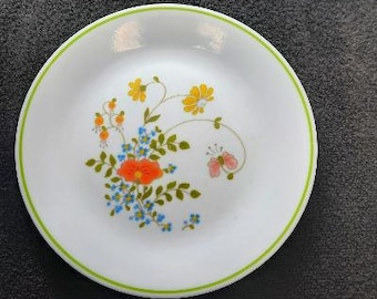 May include: A white ceramic plate with a green rim features a floral design with orange, yellow, and blue flowers and a pink butterfly.