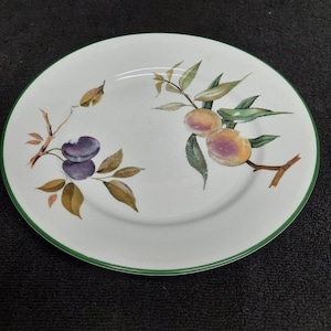 May include: A white ceramic plate with a green rim features a painted design of plums and peaches with green leaves.