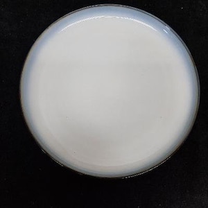 May include: A round, white ceramic plate with a light blue rim. The plate has a glossy finish and a simple, elegant design. The plate is suitable for serving food.