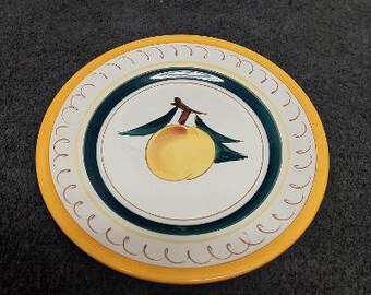 May include: A yellow ceramic plate with a blue and white border. The center of the plate features a hand-painted design of a peach with green leaves.