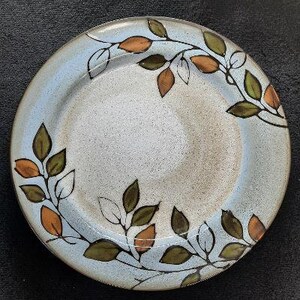 May include: A blue ceramic dinner plate with a brown and orange leaf design. The plate has a white background and a slightly raised rim.