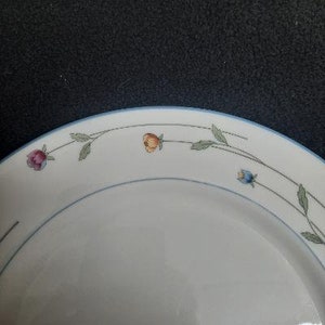 May include: White ceramic dinner plate with a blue rim and a floral design featuring pink, orange, and blue flowers.