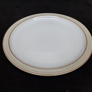 May include: A white ceramic dinner plate with a brown rim. The plate has a subtle glaze and a slightly textured surface.