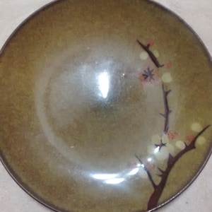May include: A brown ceramic plate with a floral design featuring a branch with white flowers and red accents.