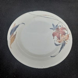 May include: A white ceramic plate with a floral design. The design features blue, brown, and red flowers with a white background.