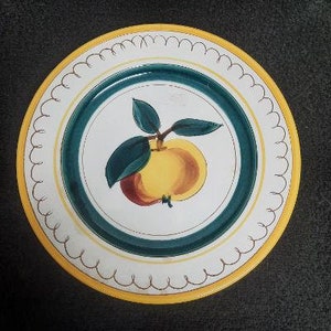 May include: A white ceramic plate with a yellow rim and a scalloped edge. The center of the plate features a green and white design with a stylized apple illustration.